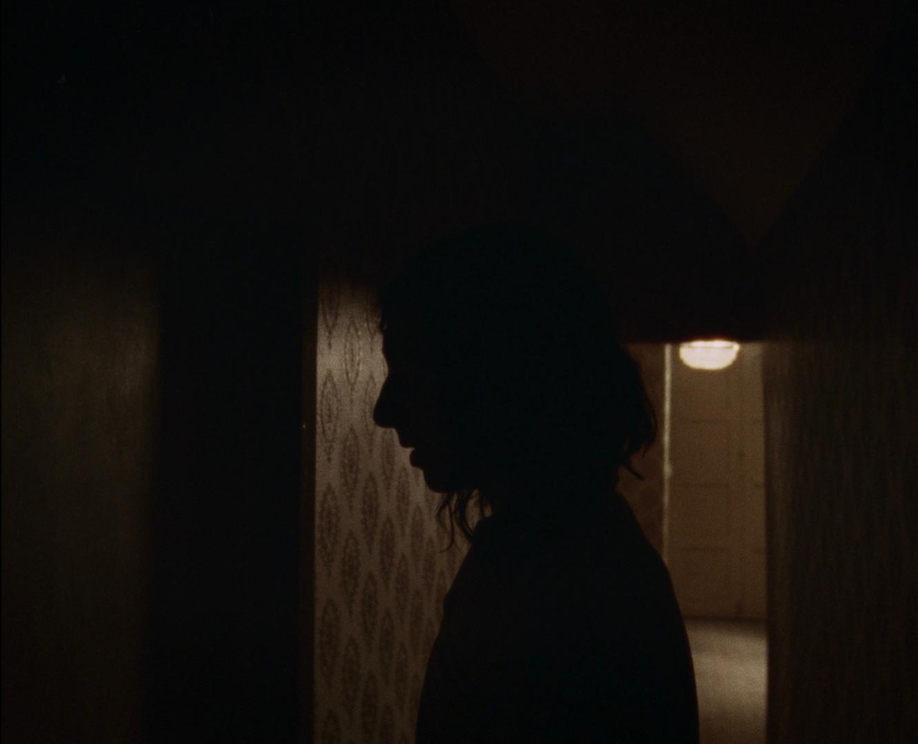 A profile in silhouette against a hallway light